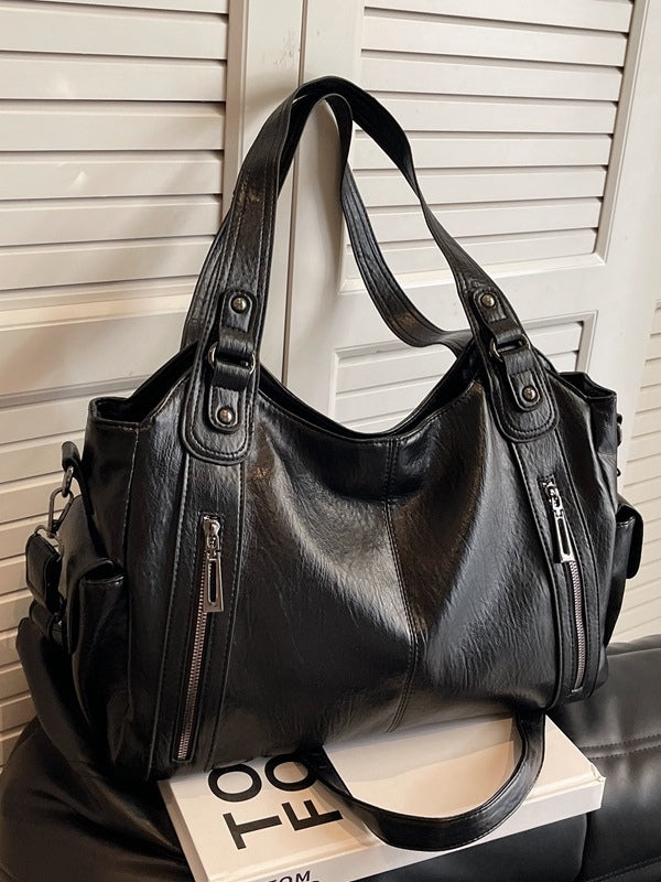 Large black rivet-studded tote bag luggage-style with zippered pocket, ideal for travelers and professionals