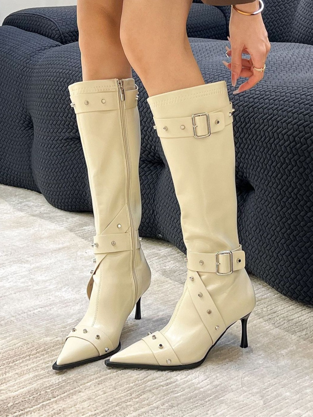 Women's black studded stiletto riding boots with pointed toe, rivet buckle details, and side zipper