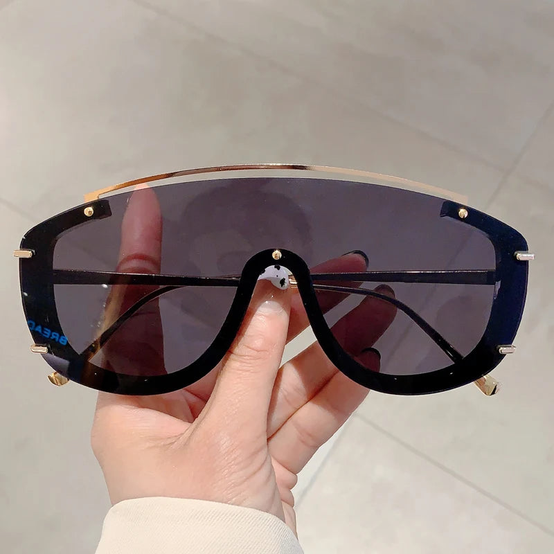Oversized shield visor sunglasses with gold-tone accents, avant-garde black frame, bold UV protection