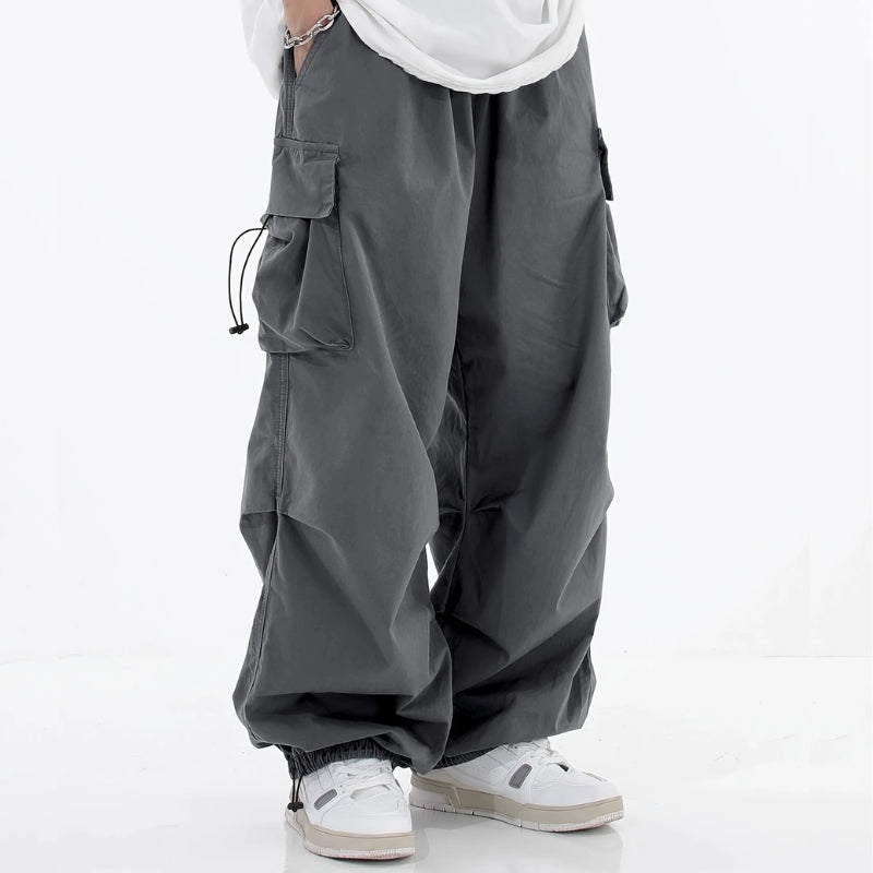 Men's wide-leg cargo pants in neutral tone with drawstring cuffs, ample utility pockets, streetwear silhouette