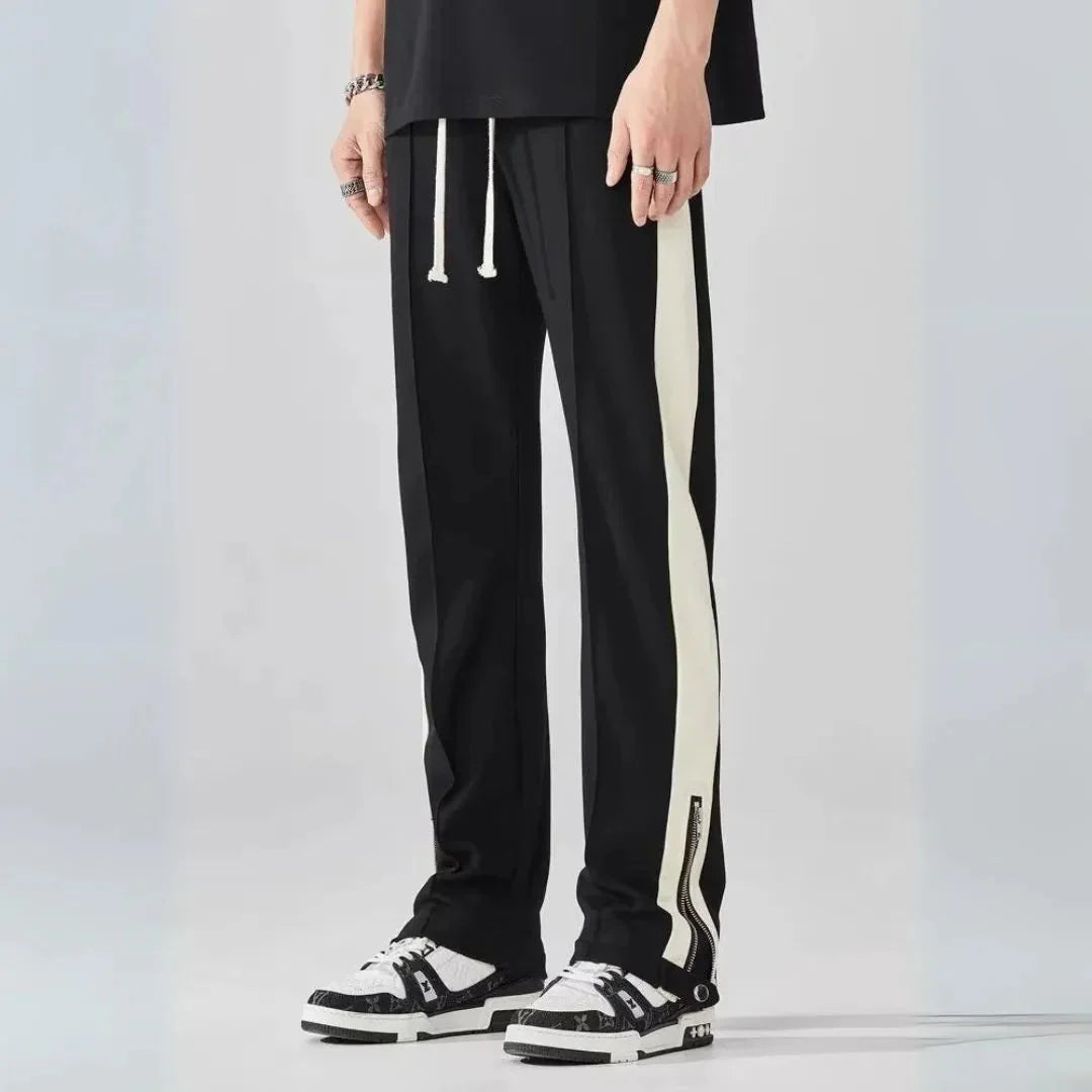 Men's black track pants with bold contrast zip detailing, adjustable drawstring waist, urban streetwear fit