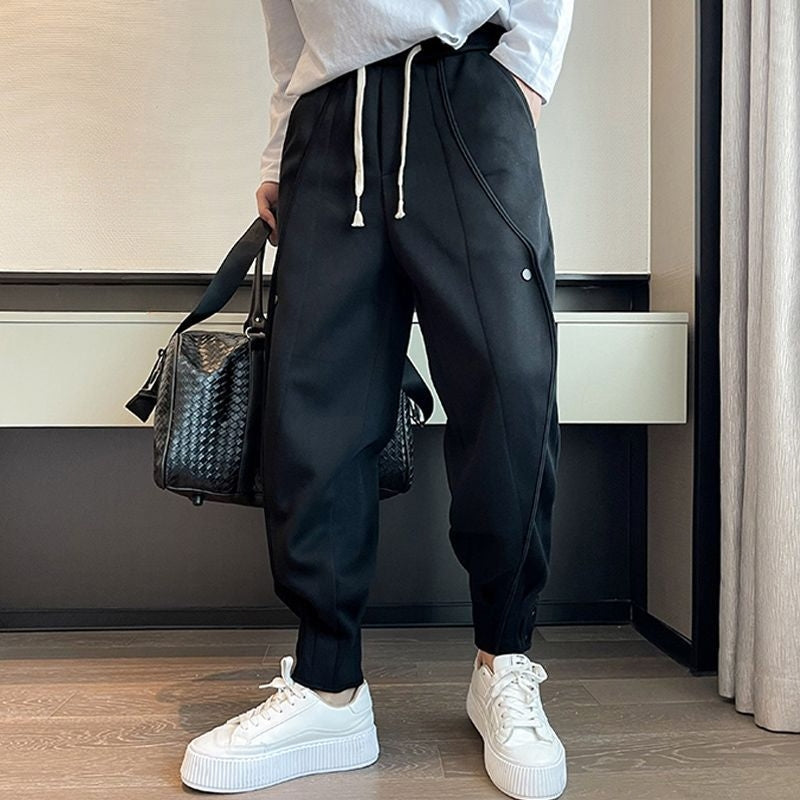 Black tapered joggers with elastic waistband and ankle button details for streetwear style