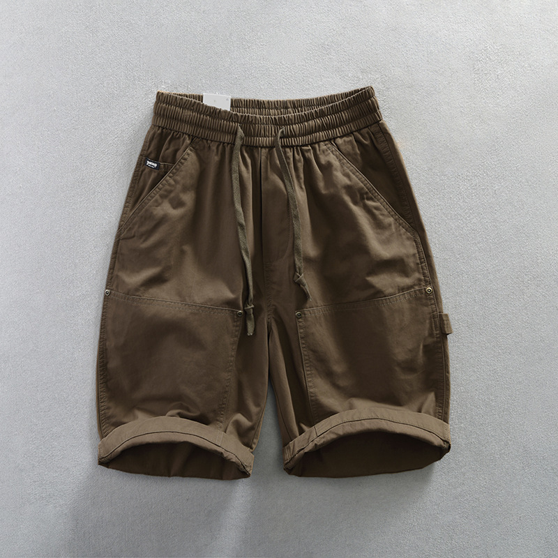 Men's beige utility twill shorts with dual pockets, elastic drawstring waist, and metal rivet accents
