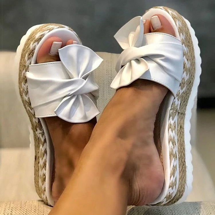 Bright yellow platform sandals with large decorative bow and woven sole, bold summer style