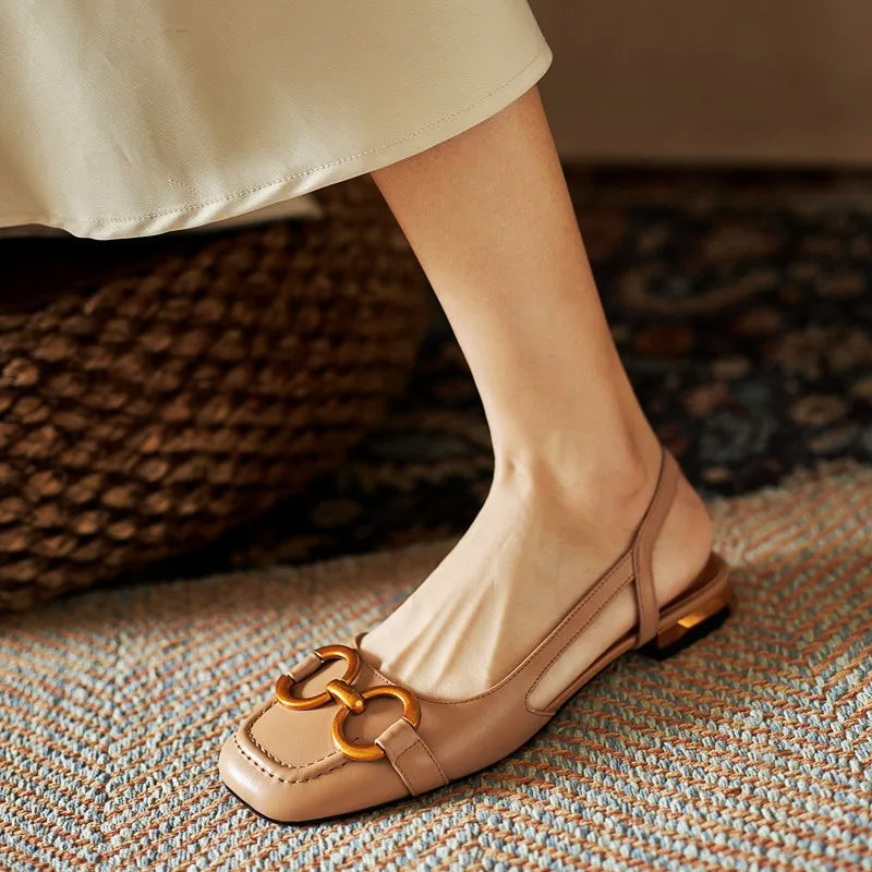 Beige sculpted slingback flats with open-back design and bold gold chain accent