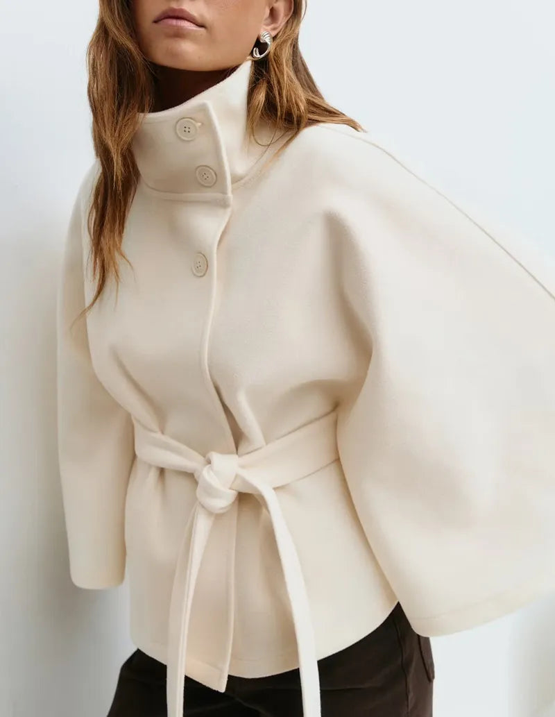 Women's spring cape coat in neutral tone with belted waist, high neck, and figure-flattering silhouette