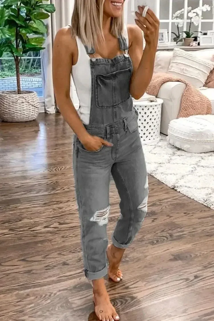 Women's relaxed fit blue denim jumpsuit with distressed knees and adjustable shoulder straps