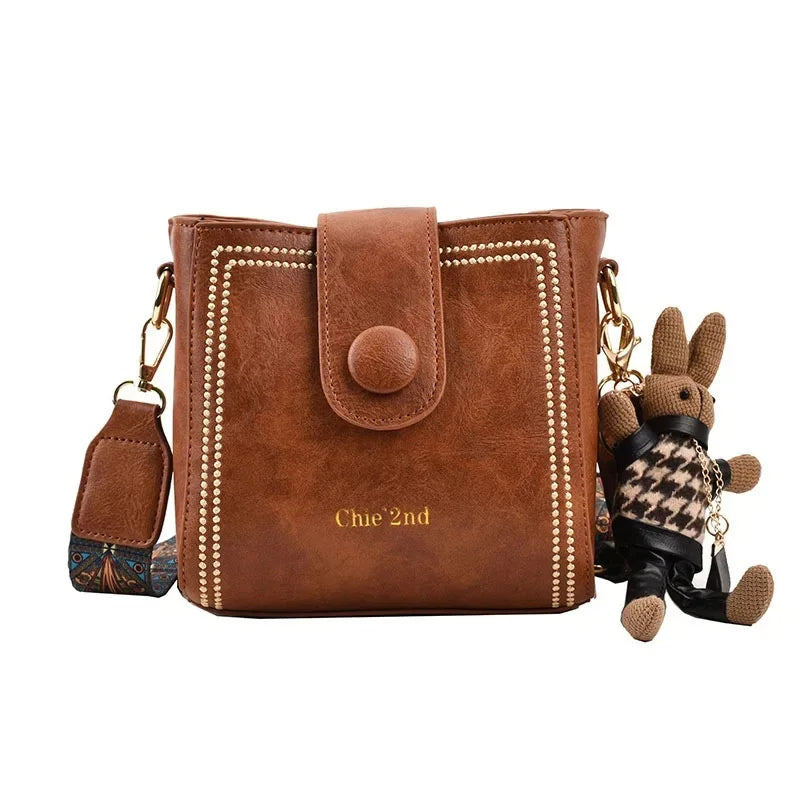 Vintage messenger crossbody bag with wide adjustable strap, muted tones and retro metal-finish hardware