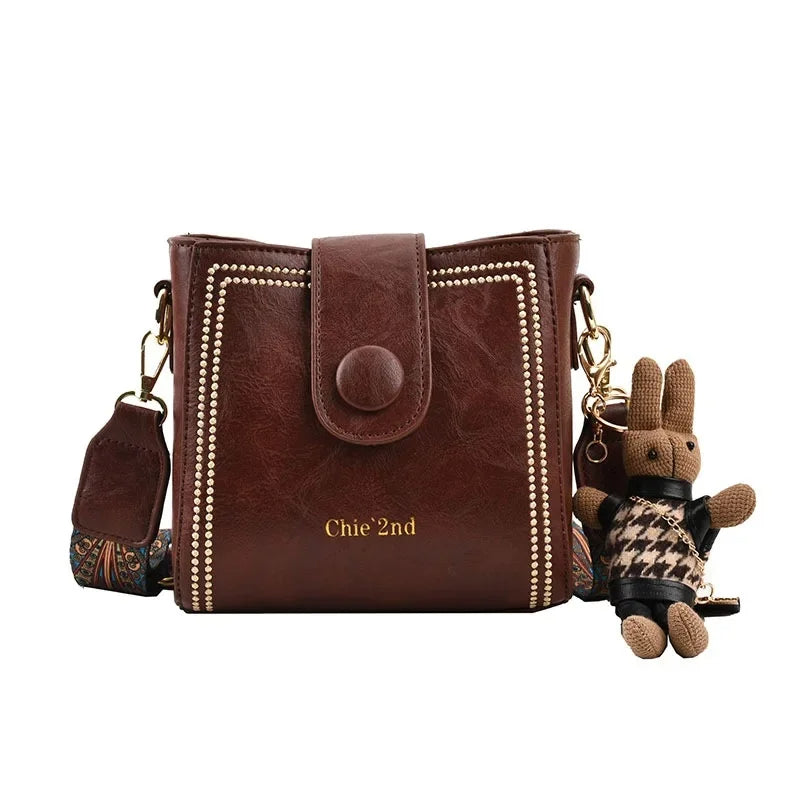 Vintage messenger crossbody bag with wide adjustable strap, muted tones and metal-finish hardware