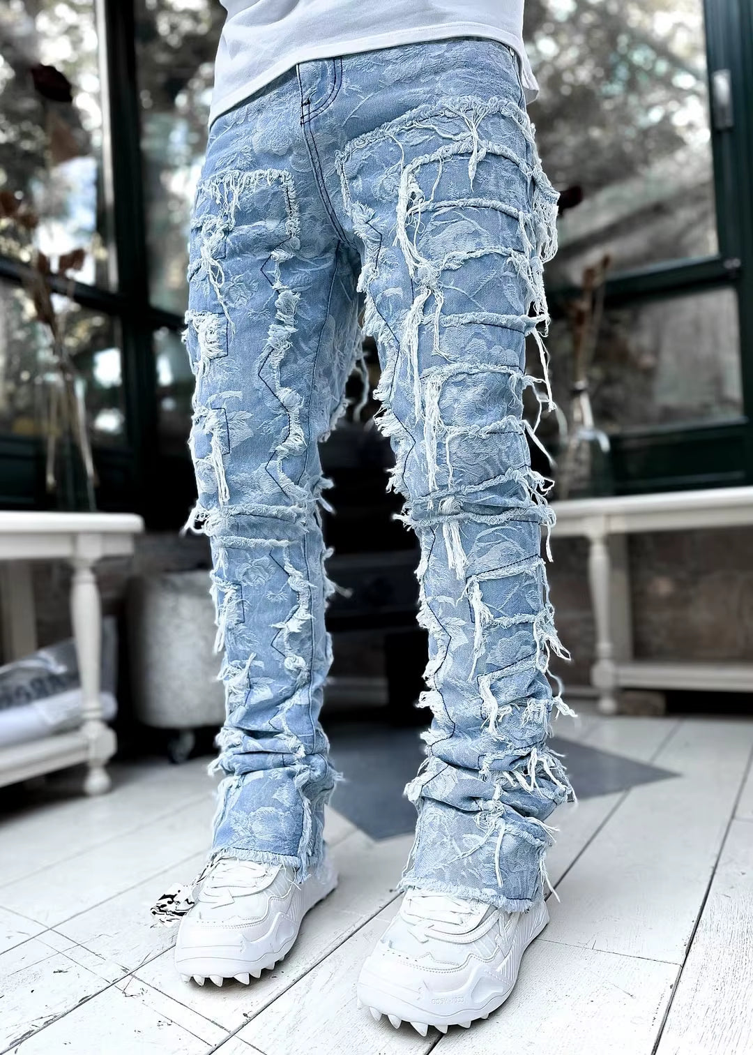 Blue distressed tapered stretch jeans with heavy fraying, reinforced seams, and layered denim streetwear detail